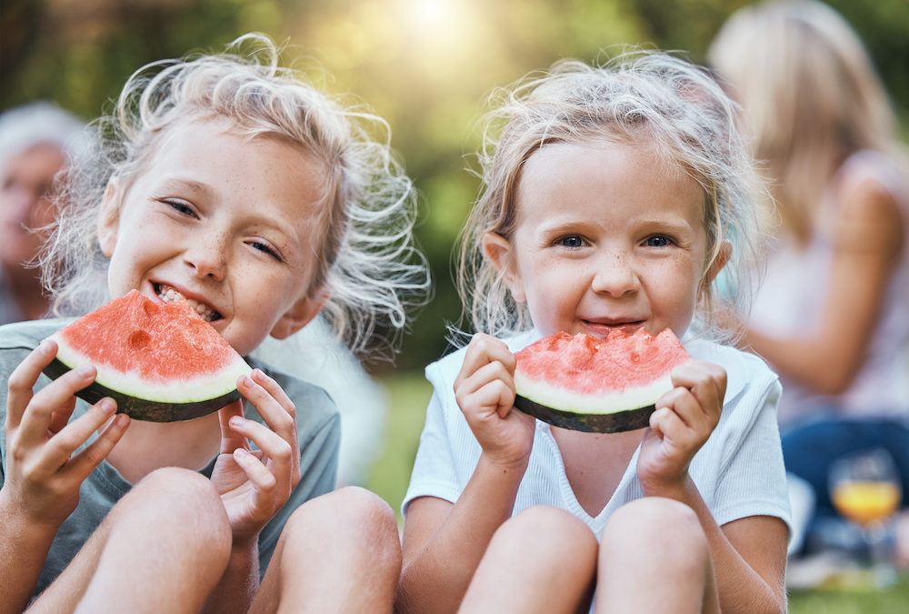 Two young girls eating Watermelon at a picnic.